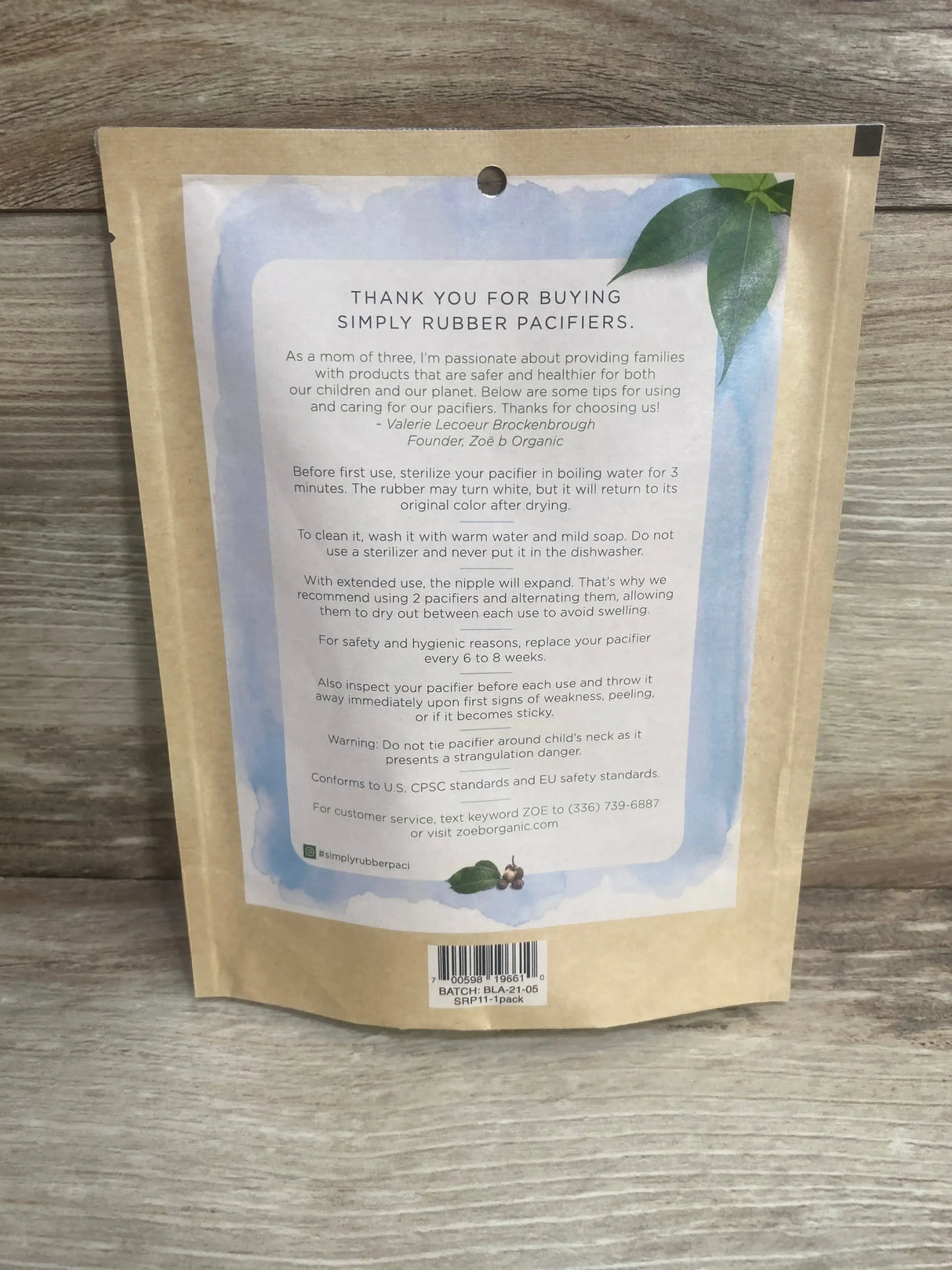 Back of Zoë b pacifier 12m kraft pouch showing Thank you for buying Simply Rubber Pacifiers headline and care info on wood