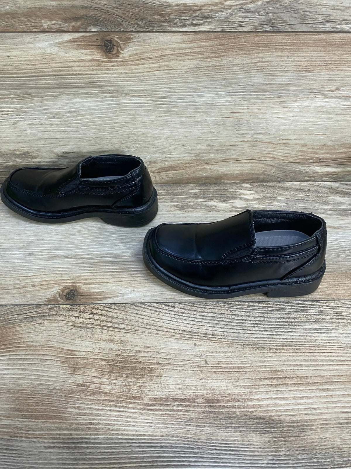 Angled side view of Deer Stags Brian slip-on black dress shoes size 9C showing smooth leather and stitched toe on wood floor