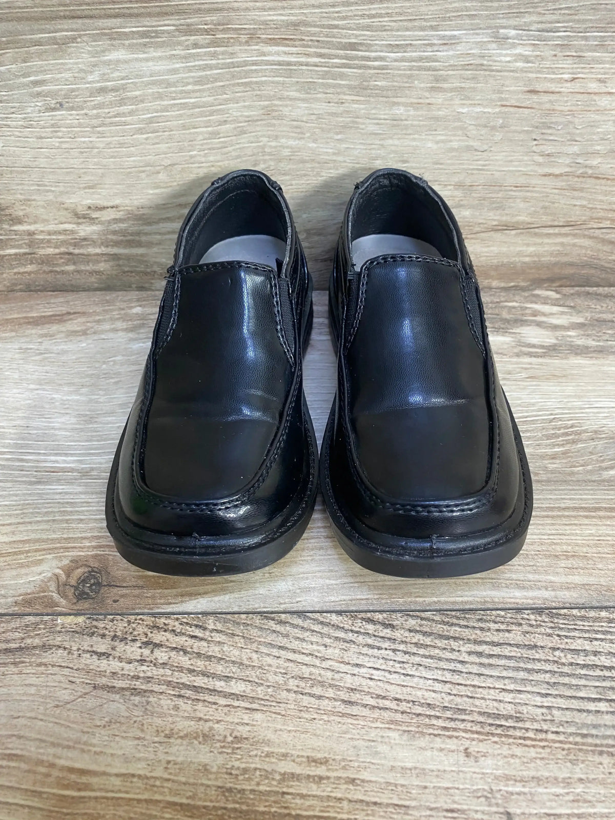 Front view of Deer Stags Brian slip-on black toddler dress shoes showing stitched square toe on wood floor background