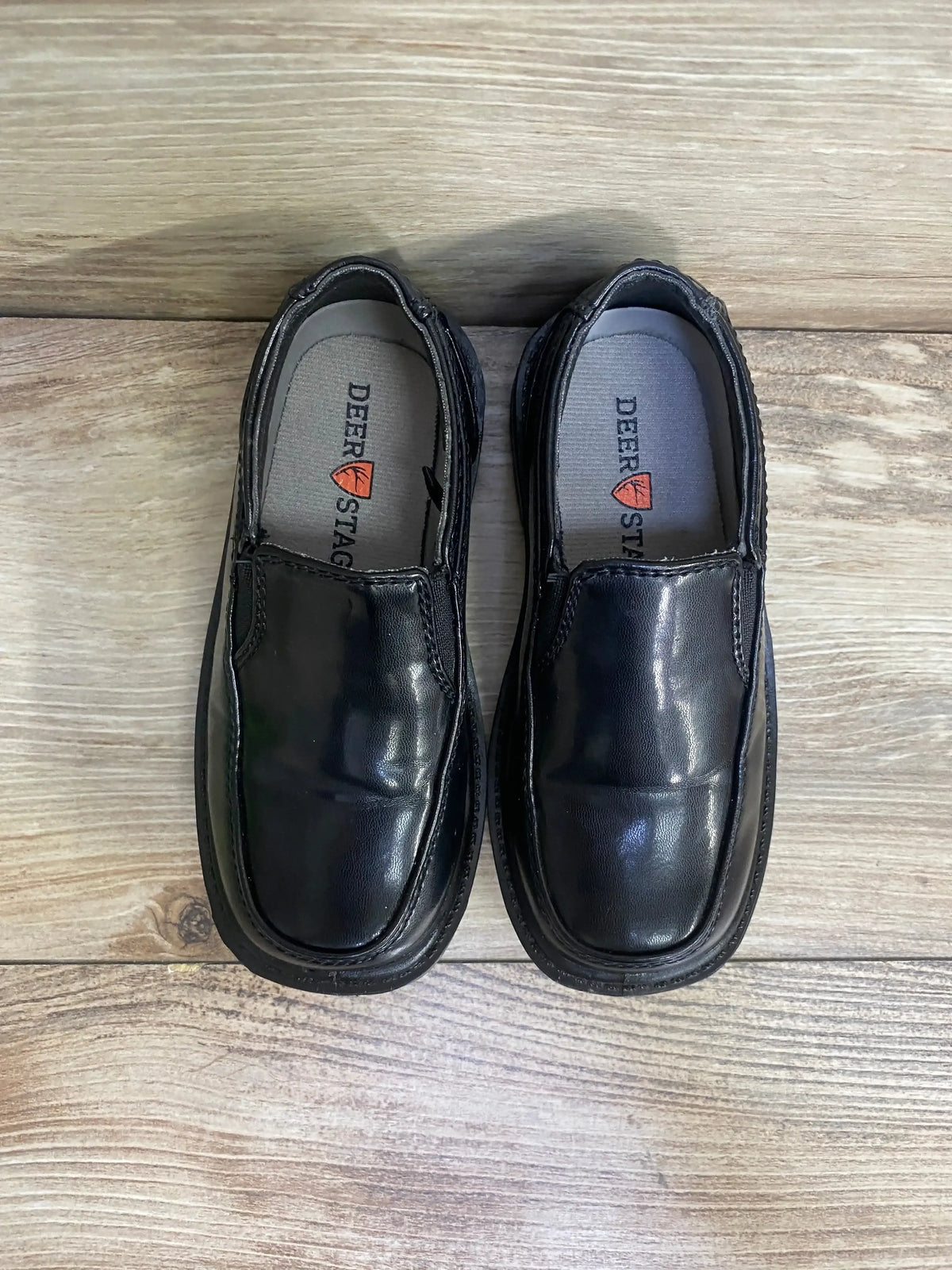 Top view of Deer Stags black slip-on dress shoes showcasing shiny finish and moc-toe stitching on light wood floor