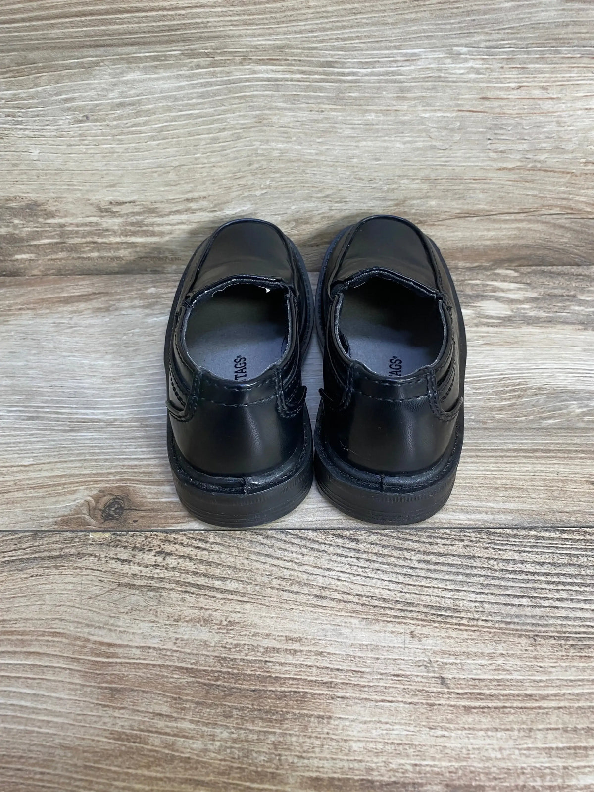 Rear view of Deer Stags Brian black slip-on kids dress shoes size 9C showing stitched heels and slip-on openings on light wood floor background