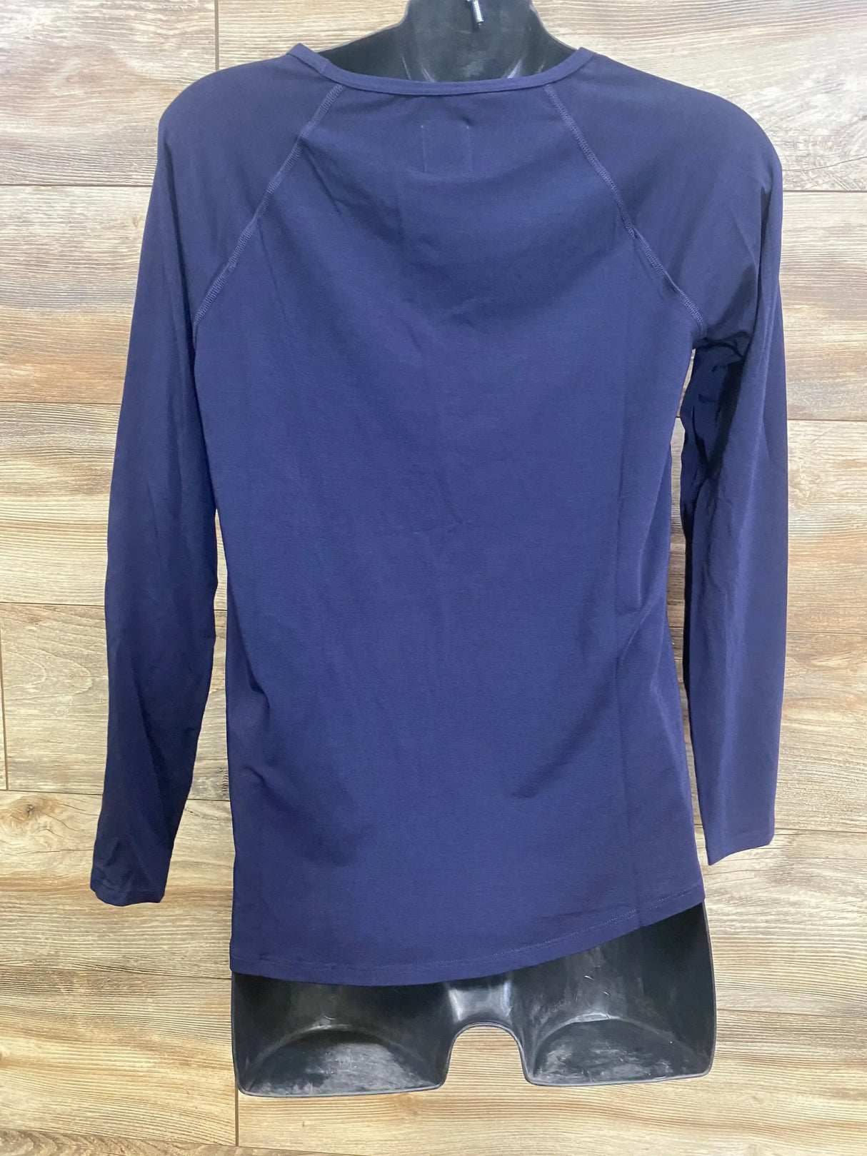 Back of navy Gap maternity Breathe long-sleeve shirt on mannequin showing raglan seams and stretch fabric, wood backdrop