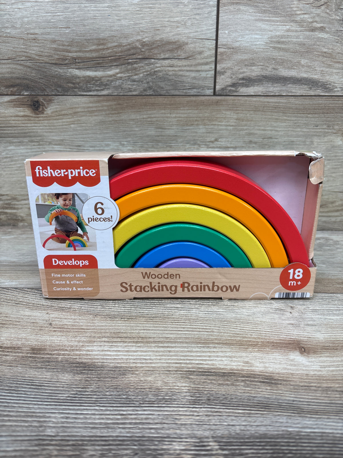 Front view of Fisher-Price wooden stacking rainbow toy showing six colorful arches in its box on a wood-grain background
