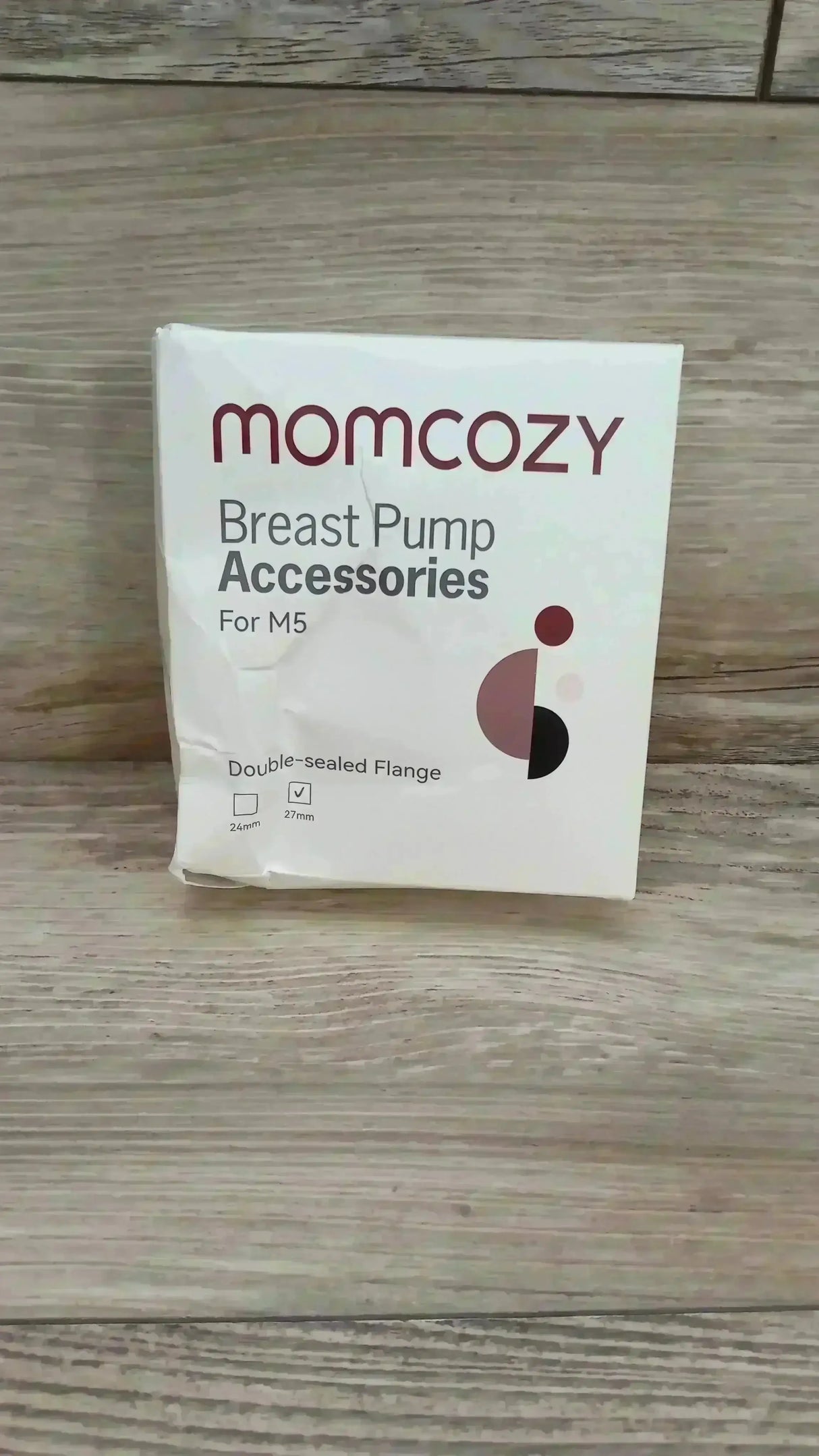 Front view of Momcozy double-sealed flange (27mm) packaging showing Breast Pump Accessories text and checked 27mm size box on light wood background