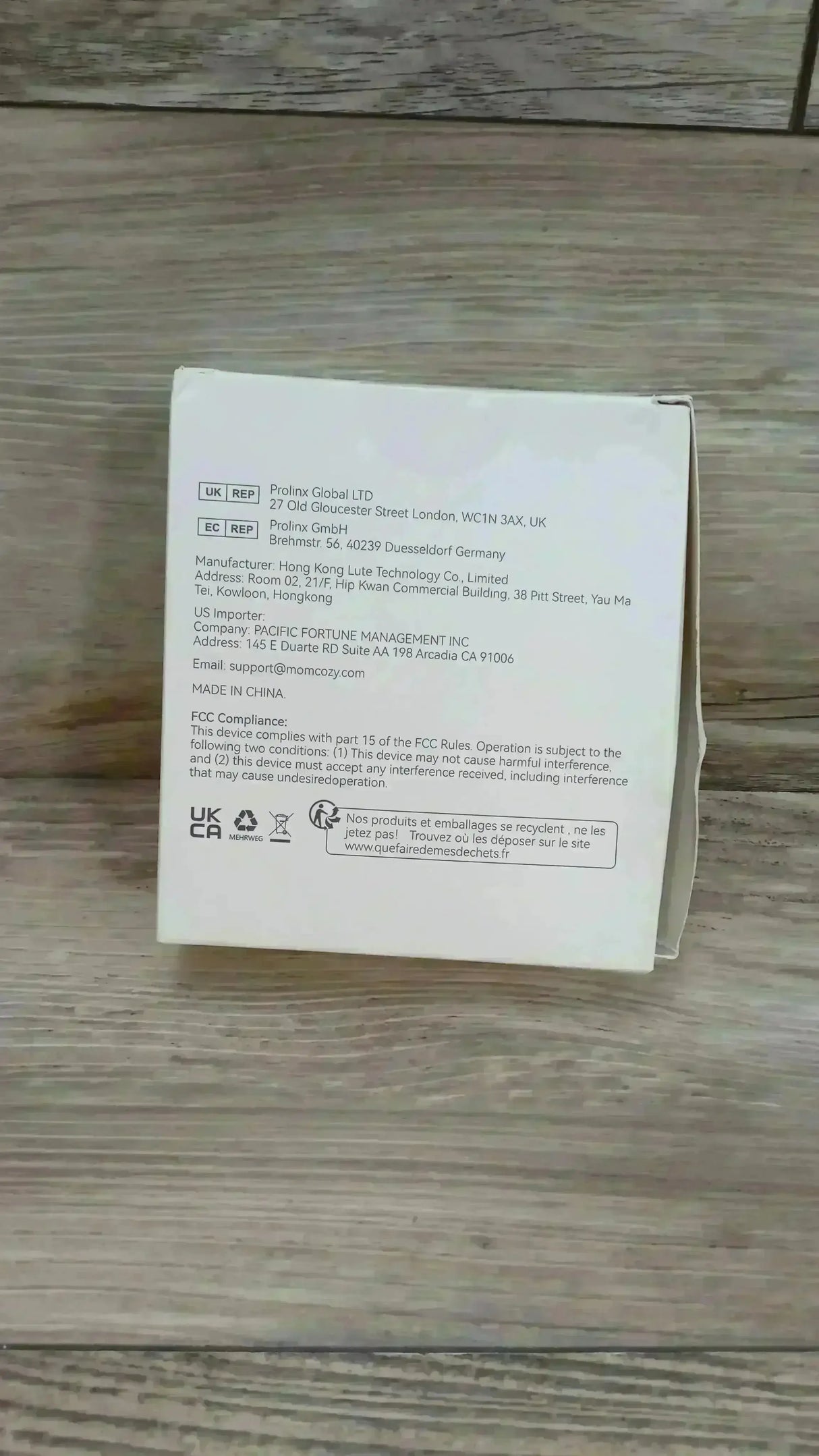 Rear view of NEW Momcozy double-sealed flange 27mm box showing manufacturer and FCC/UKCA compliance text and recycling symbols on a wooden floor