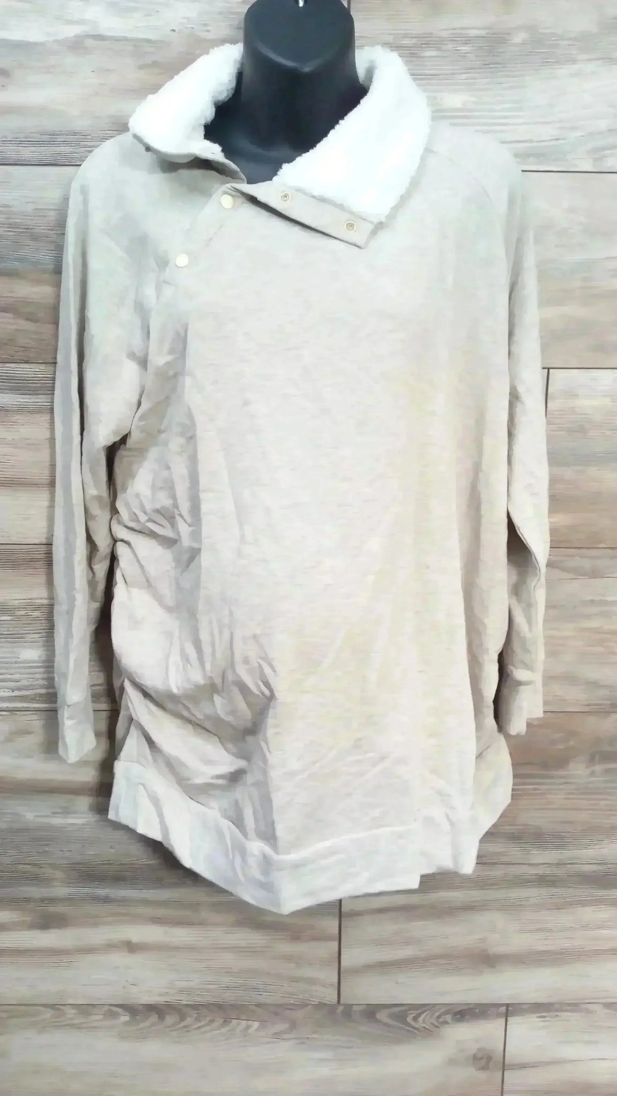 Front view of oatmeal maternity sweatshirt with sherpa snap collar and ruched sides on black mannequin, wood background