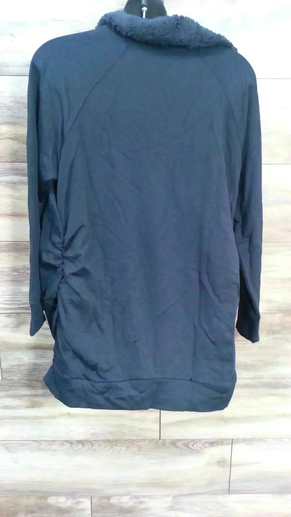 Back view of navy Isabel maternity sweatshirt showcasing sherpa snap collar and side ruching on light wood background