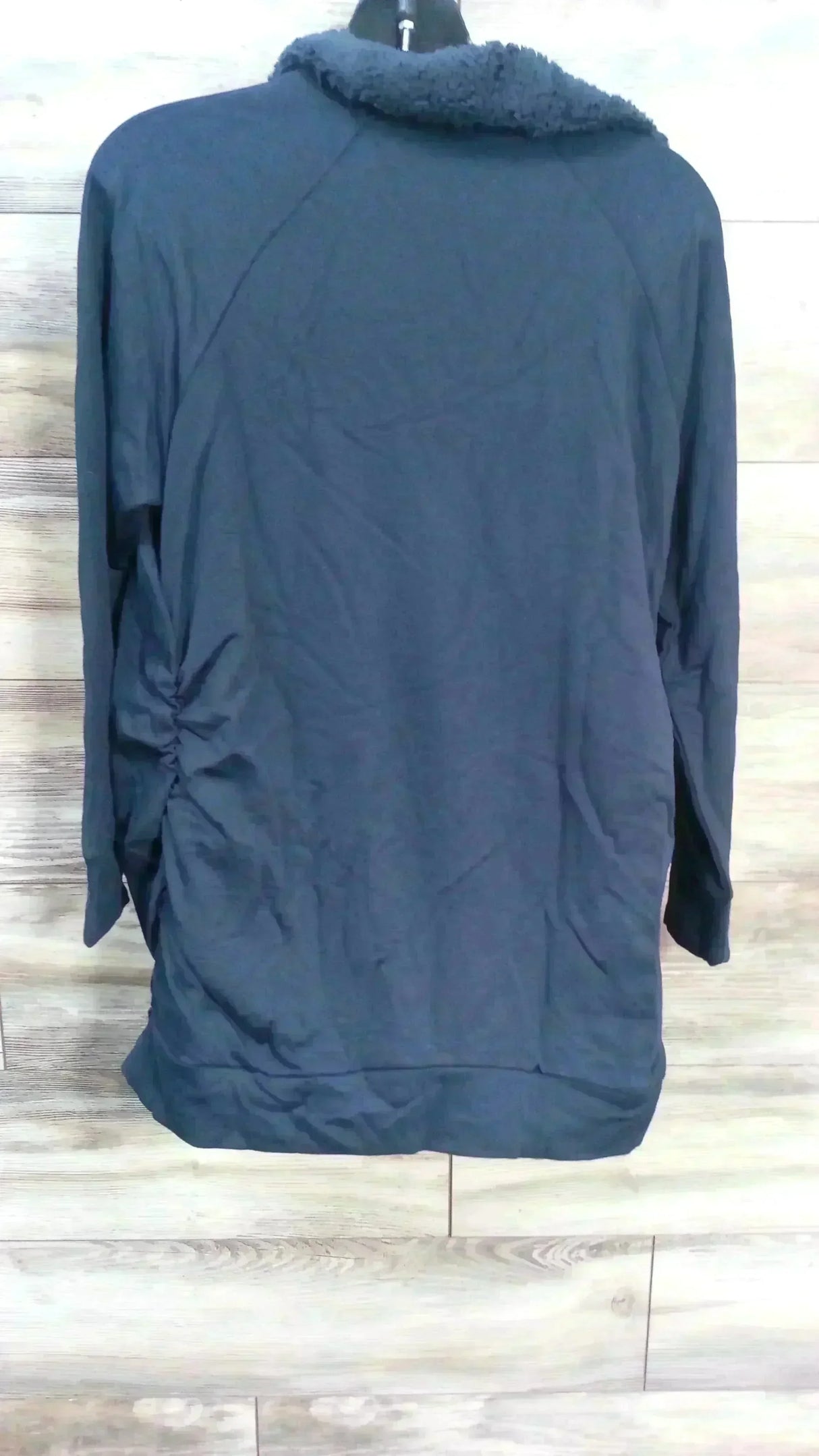 Back view of navy Isabel maternity sweatshirt showcasing sherpa snap collar and side ruching on light wood background