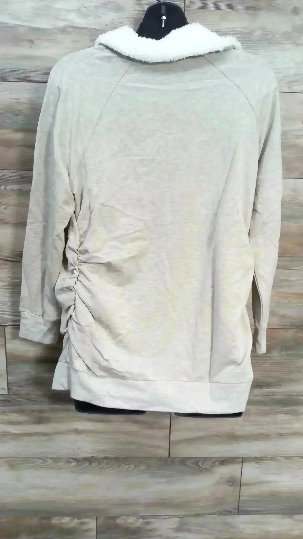 Back view of oatmeal Isabel maternity sweatshirt with white sherpa collar and side ruching, on wood-plank background
