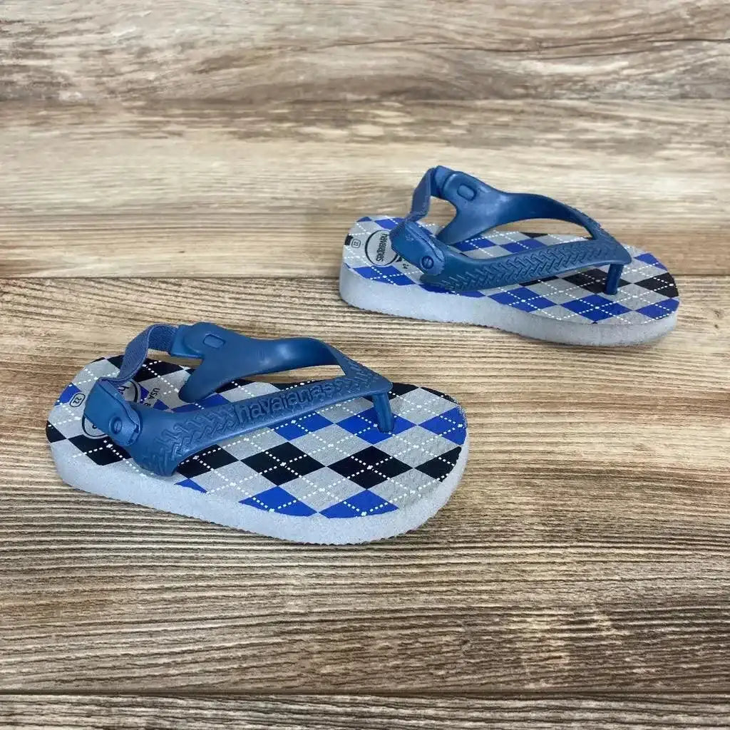 Angled view of Havaianas flip flops size 8C showcasing blue elastic backs and argyle footbeds on a wood surface