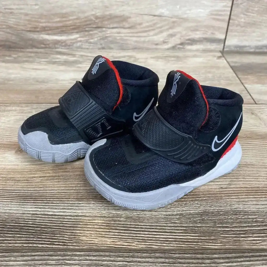 Front three-quarter view of black Nike Kyrie 6 toddler sneakers, size 4C, showing midfoot strap and white sole on wood floor