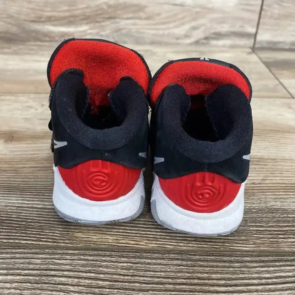 Rear view of kids' Nike Kyrie 6 sneakers, size 4C, showing black upper, red circular heel detail and red lining on wood floor
