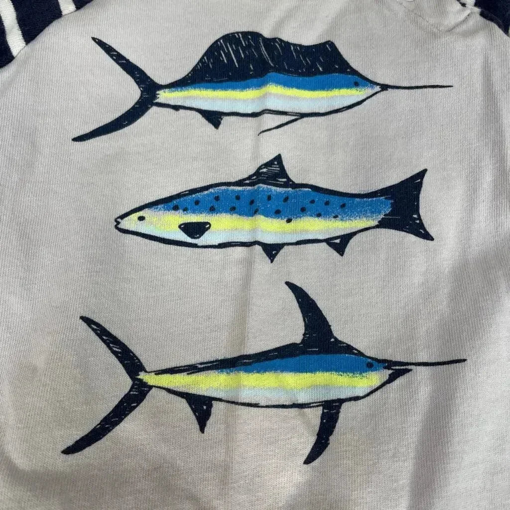 Front close-up of Tea Collection coverall showing three striped fish prints in navy and yellow on light gray fabric