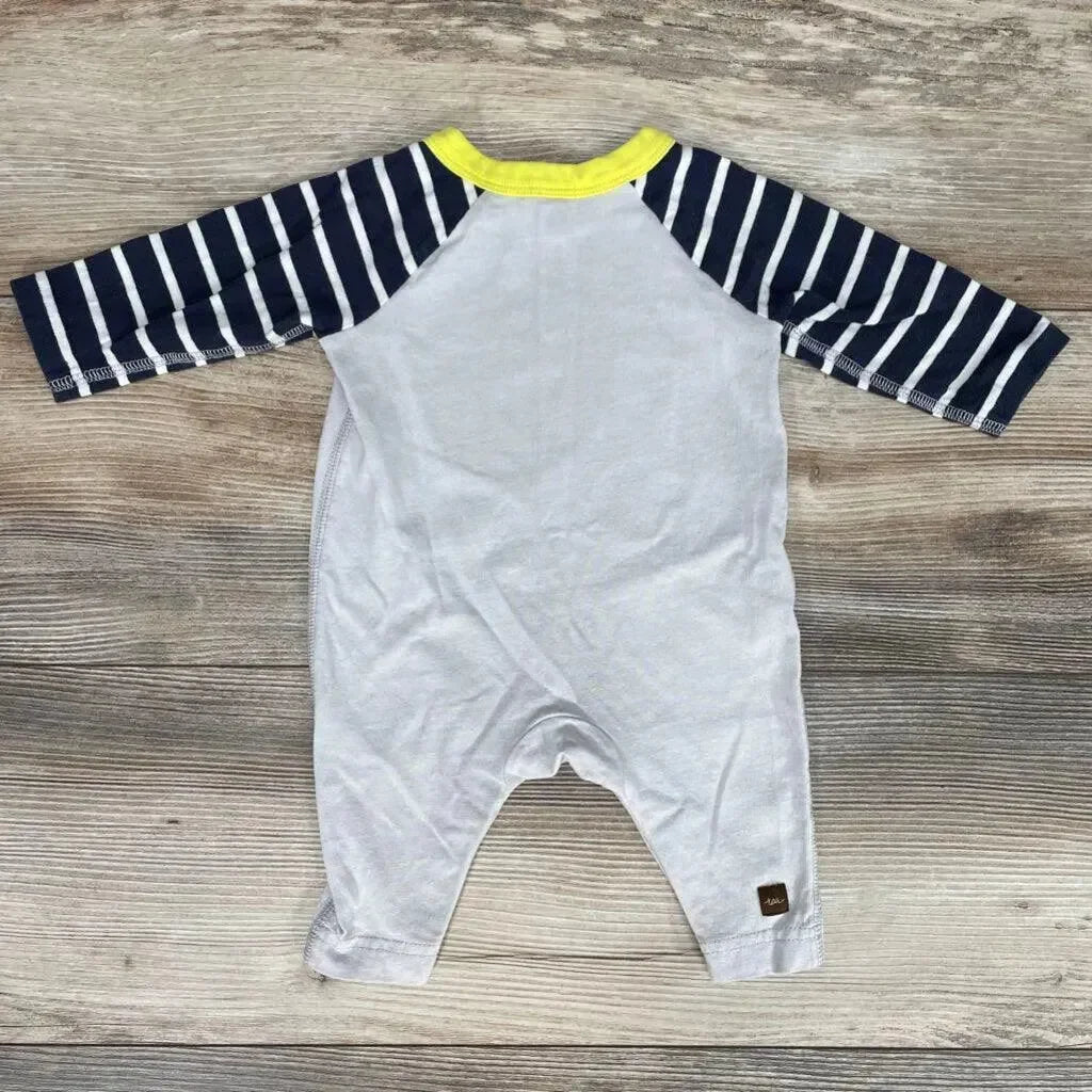 Back view of Tea Collection striped fish coverall with navy-and-white sleeves, yellow neck trim, light gray body on wood