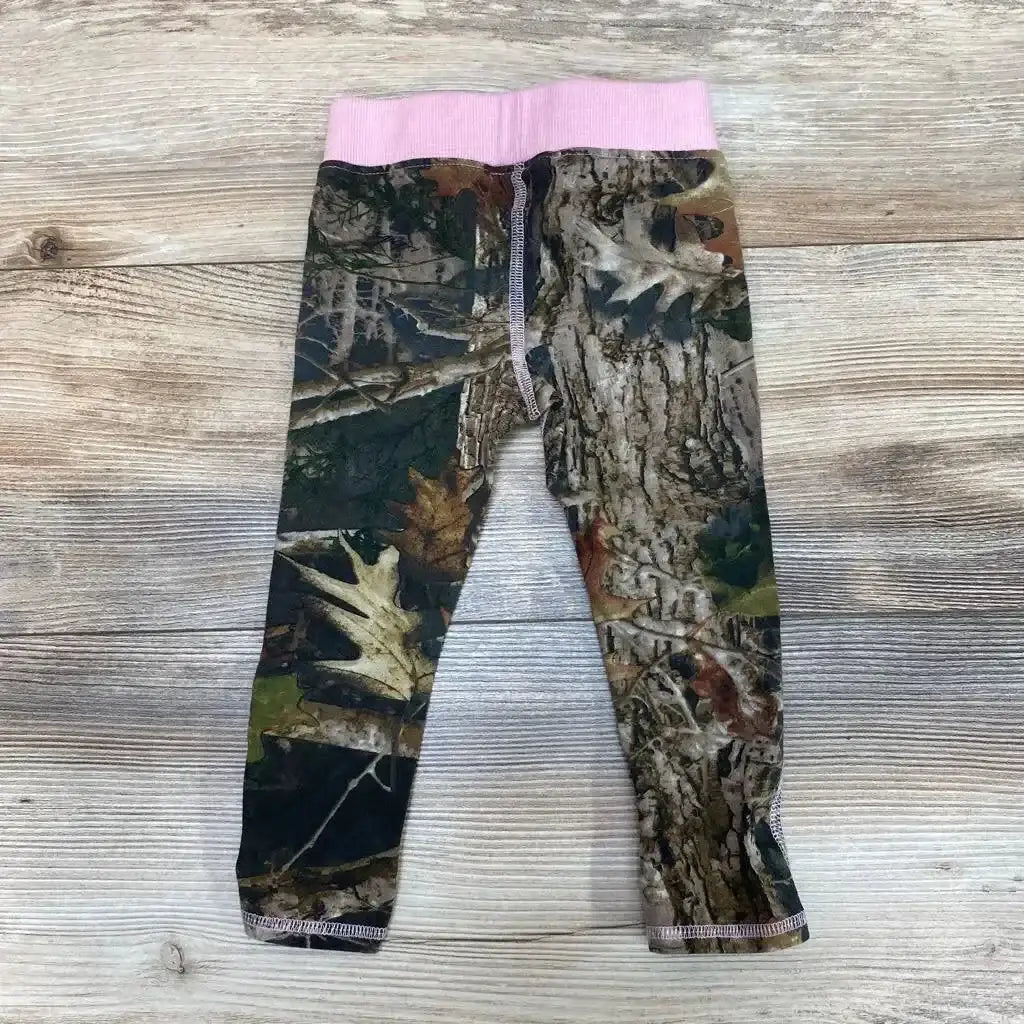 Flat lay of toddler 2T outdoor leggings showcasing camouflage print and pink elastic waistband on wood plank background