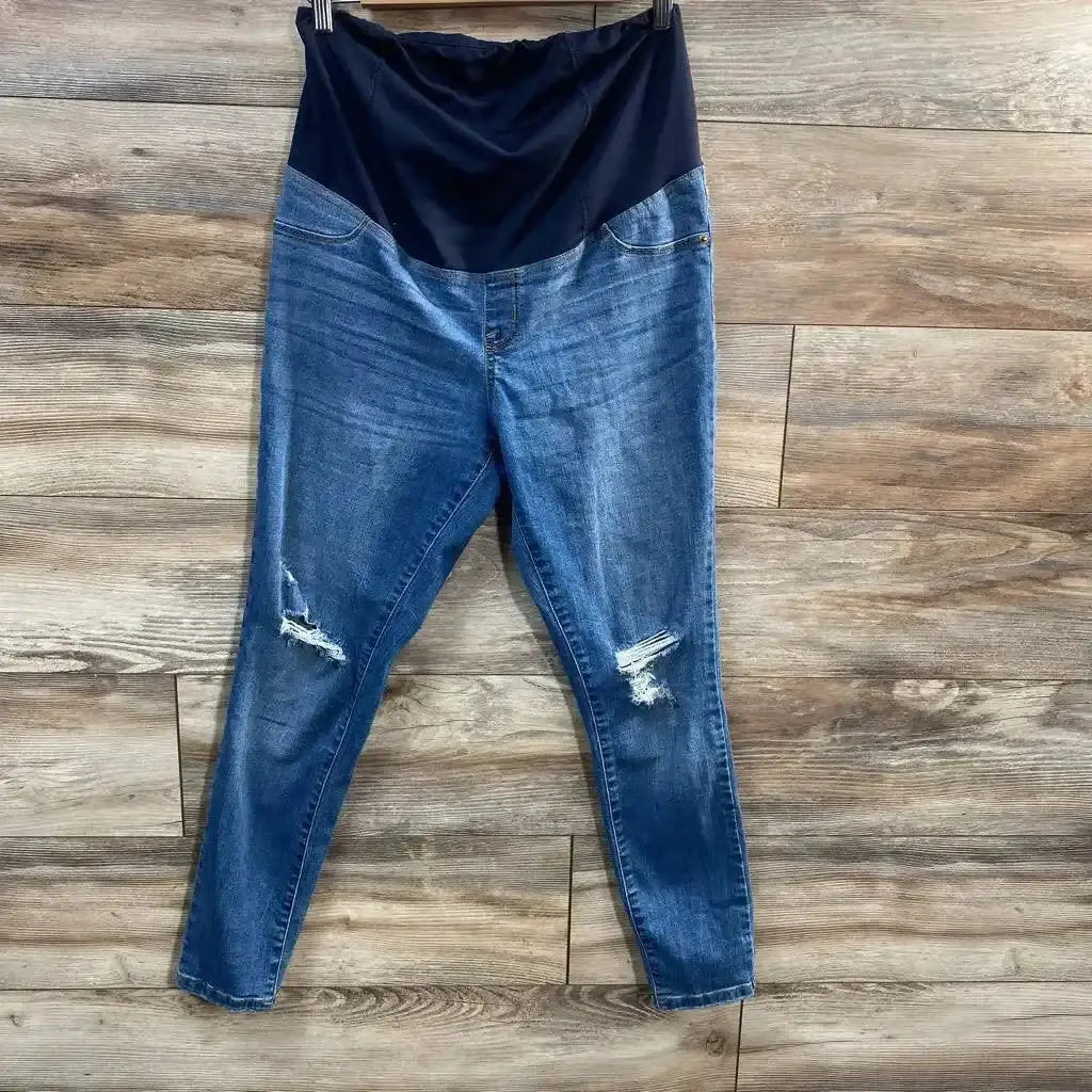 Front view of Isabel maternity crossover-panel distressed skinny jeans showcasing black crossover belly panel and ripped knees on wood floor background