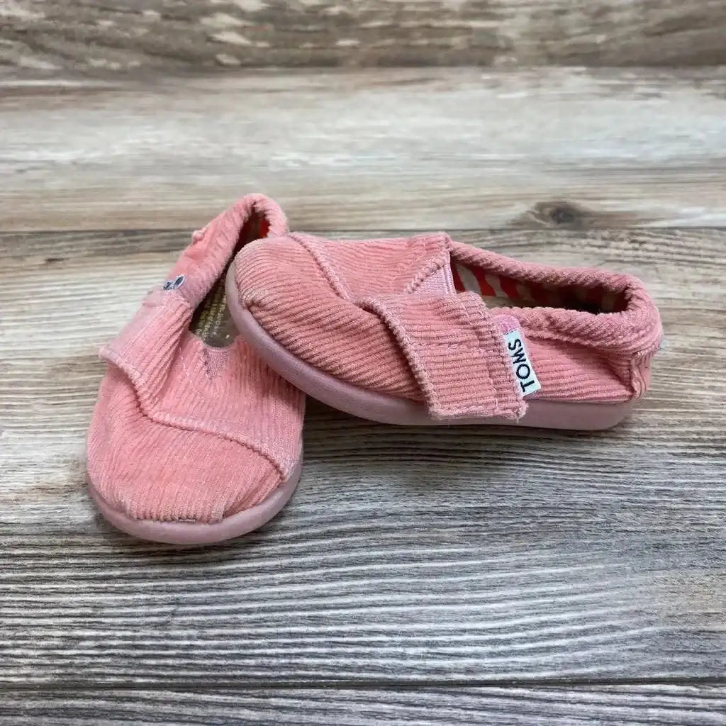 Angled view of Toms Slip On Canvas Shoes in coral pink corduroy showcasing brand tag and elastic vamp on wood plank floor