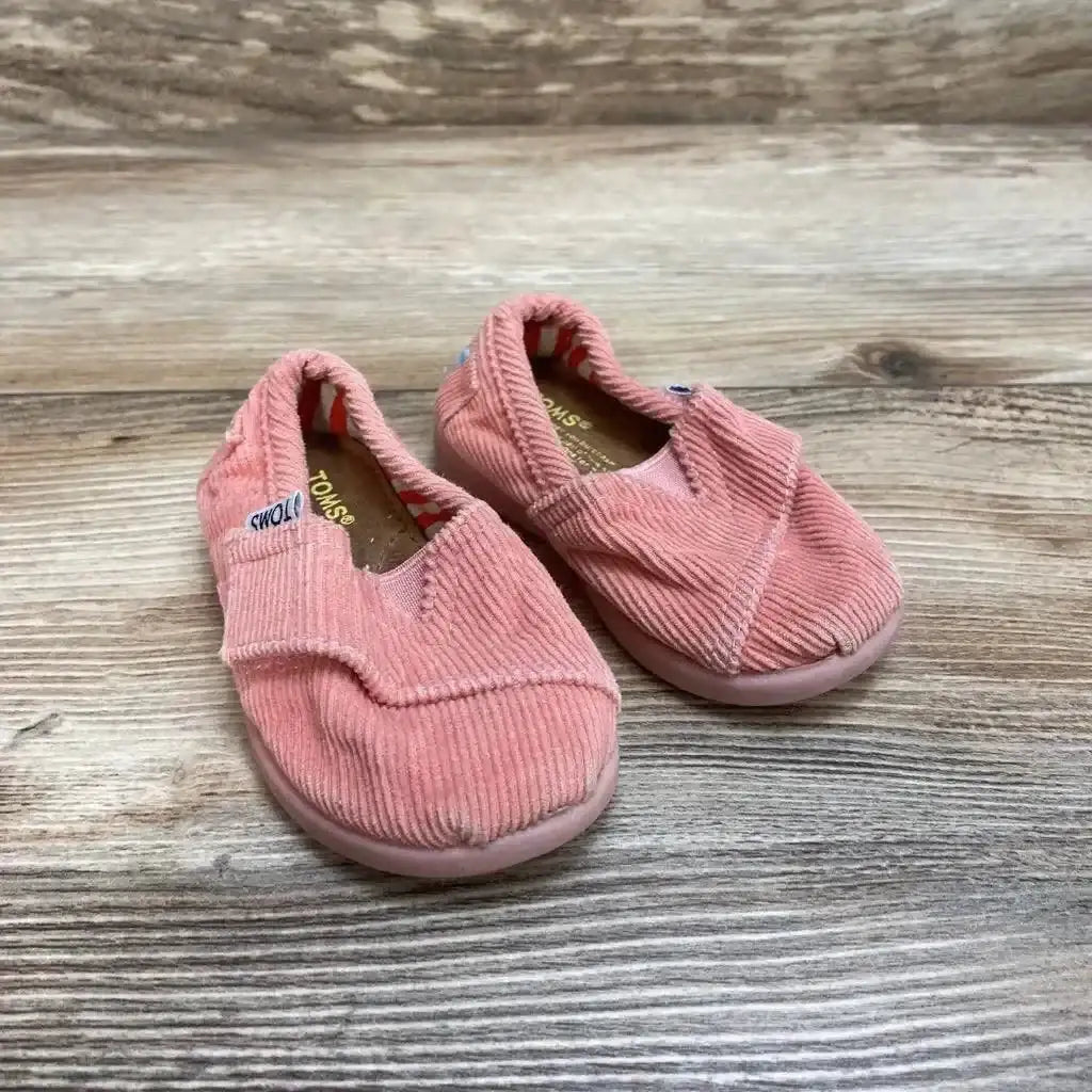Three-quarter view of pink corduroy Toms slip-on toddler shoes (size 3C) showcasing elastic gore and wear on wood floor