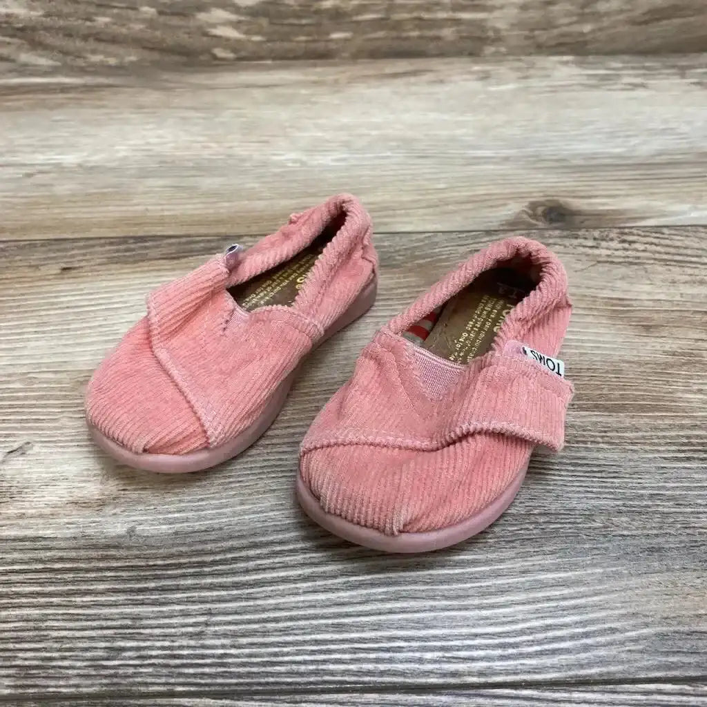 Front three-quarter view of pink toddler TOMS slip-on corduroy shoes (size 3C) showing Velcro strap on wood floor