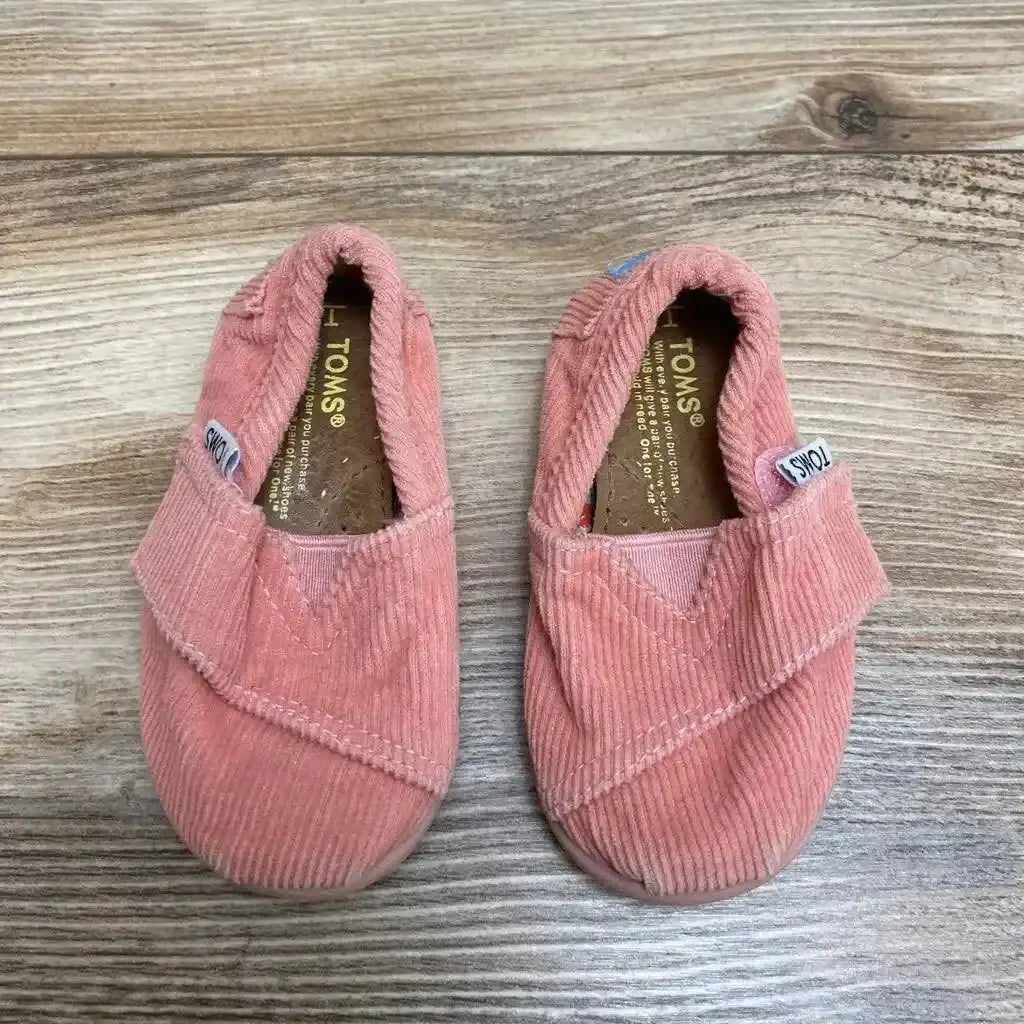 Top view of pink corduroy TOMS slip-on shoes size 3C showing elastic gore and worn insoles on wood floor