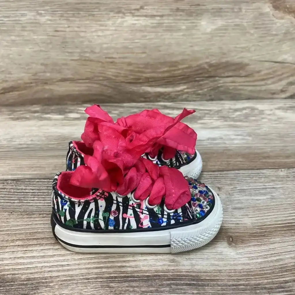 Side view of Converse Chuck Taylor Low Top Sneakers size 2c showcasing zebra print canvas with rhinestone embellishments and pink ribbon laces on wood plank floor