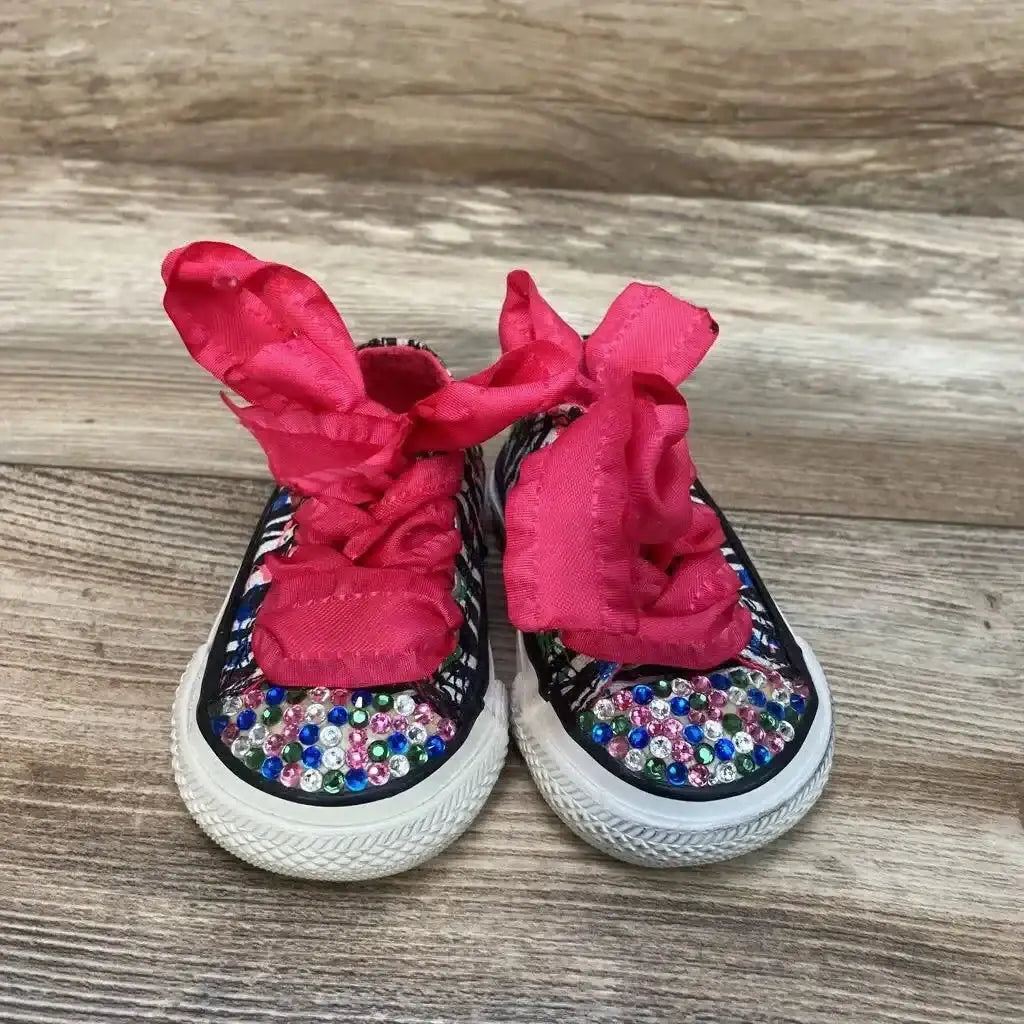Front view of toddler pink Converse low-top sneakers size 2C with multicolor rhinestones and wide pink ribbon laces on wood floor