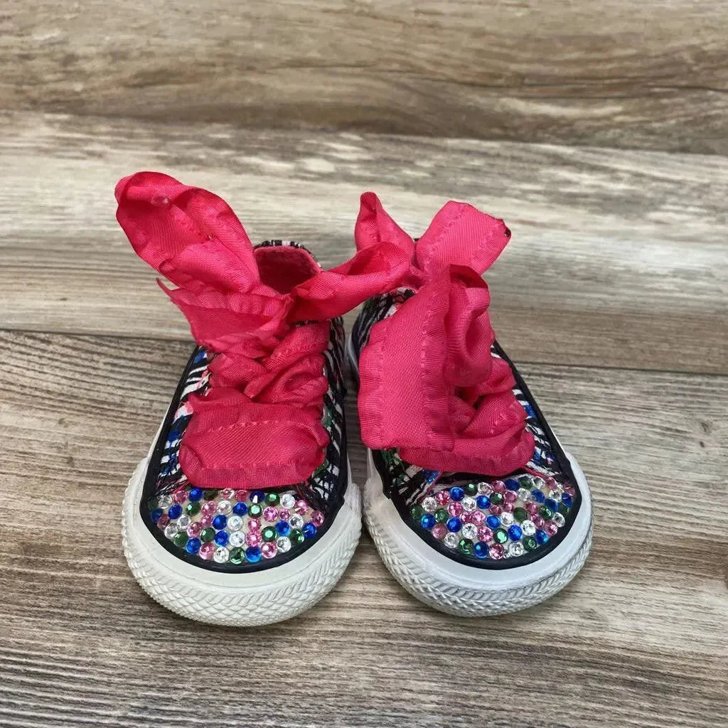 Front view of toddler pink Converse low-top sneakers size 2C with multicolor rhinestones and wide pink ribbon laces on wood floor