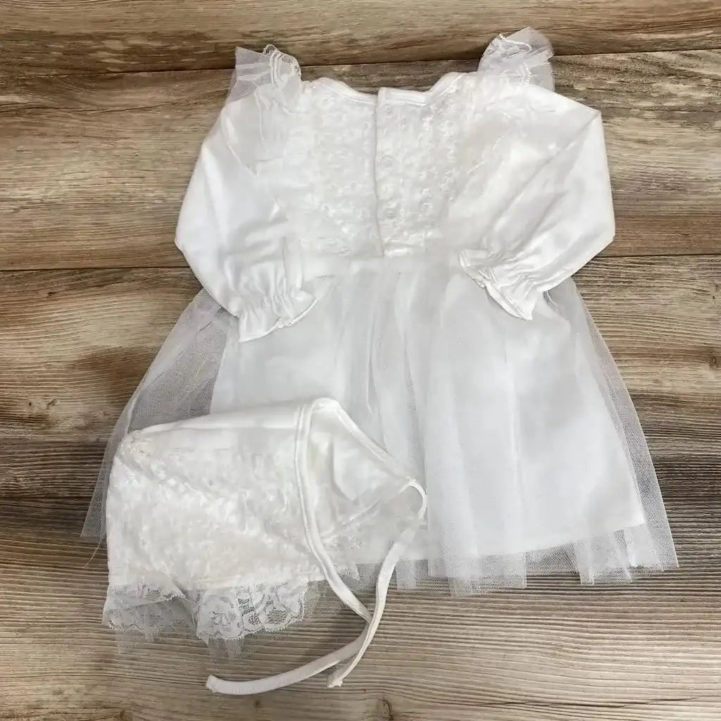 Flat lay of white tulle overlay long sleeve dress with lace bodice and matching lace bonnet on wood plank floor