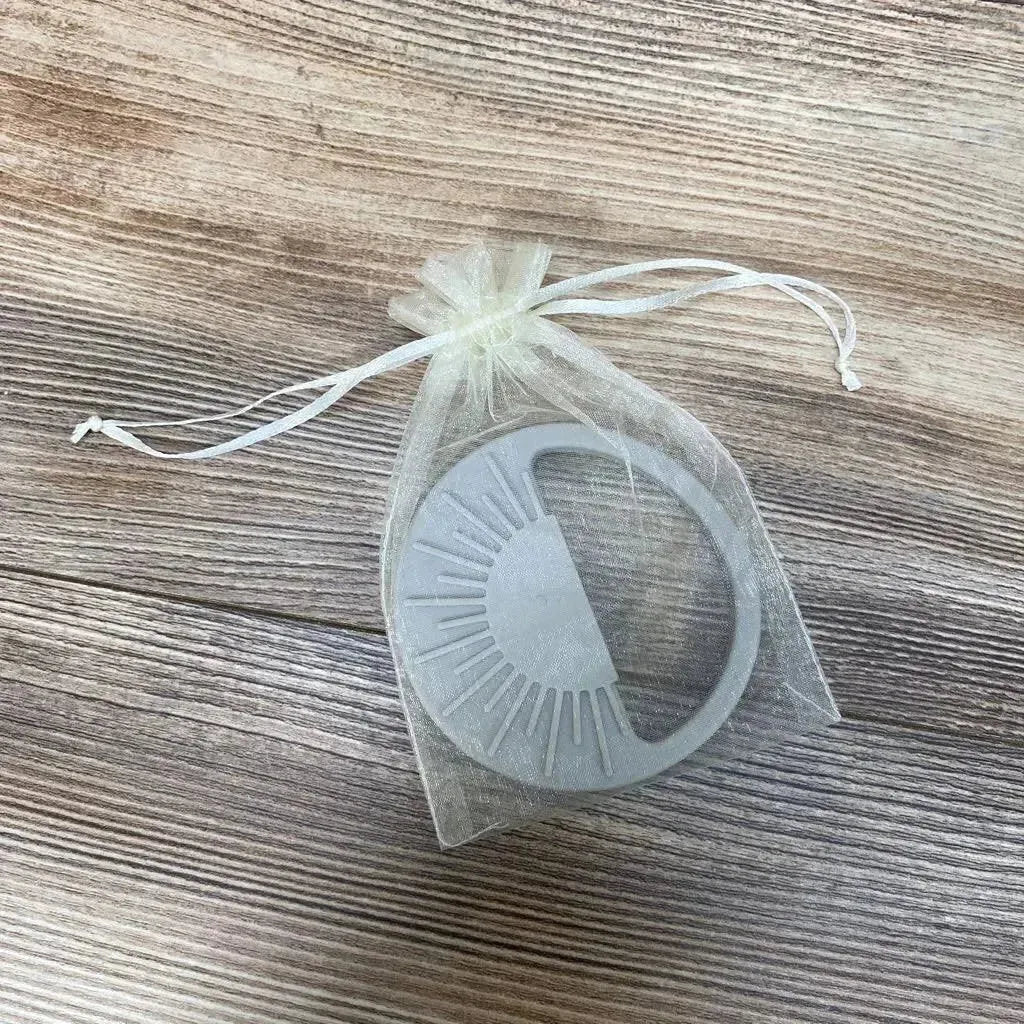 Top-down view of Avery & Everett grey silicone teether with textured ridges in a sheer organza pouch on wood surface