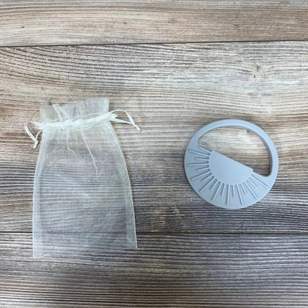 Top view of Avery & Everett grey silicone teether showing textured sunburst chewing ridges with organza pouch on wood surface