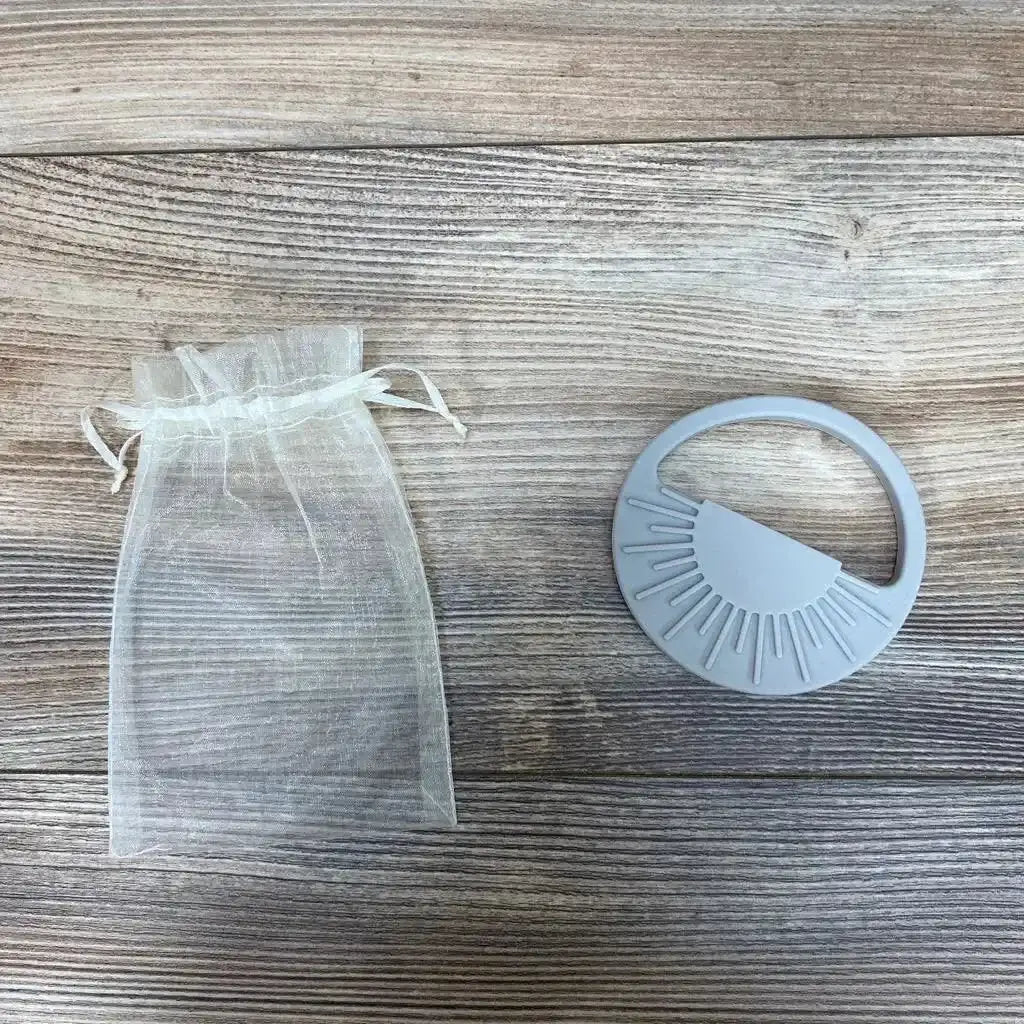 Top view of Avery & Everett grey silicone teether showing textured sunburst chewing ridges with organza pouch on wood surface