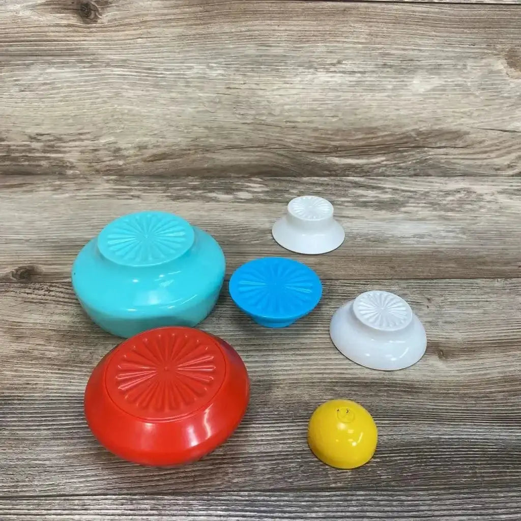 Top-down view of Kid O Rounded Stackers showing six rounded stacking cups (red, teal, blue, two white, yellow) on a wood background