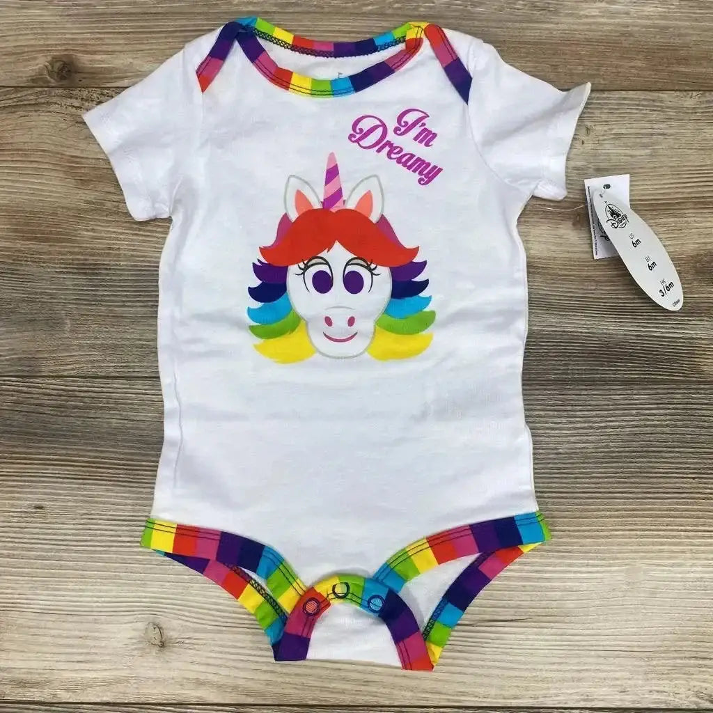 Flat lay of white 6M baby bodysuit with rainbow trim, unicorn face print and I'm Dreamy text on wooden background