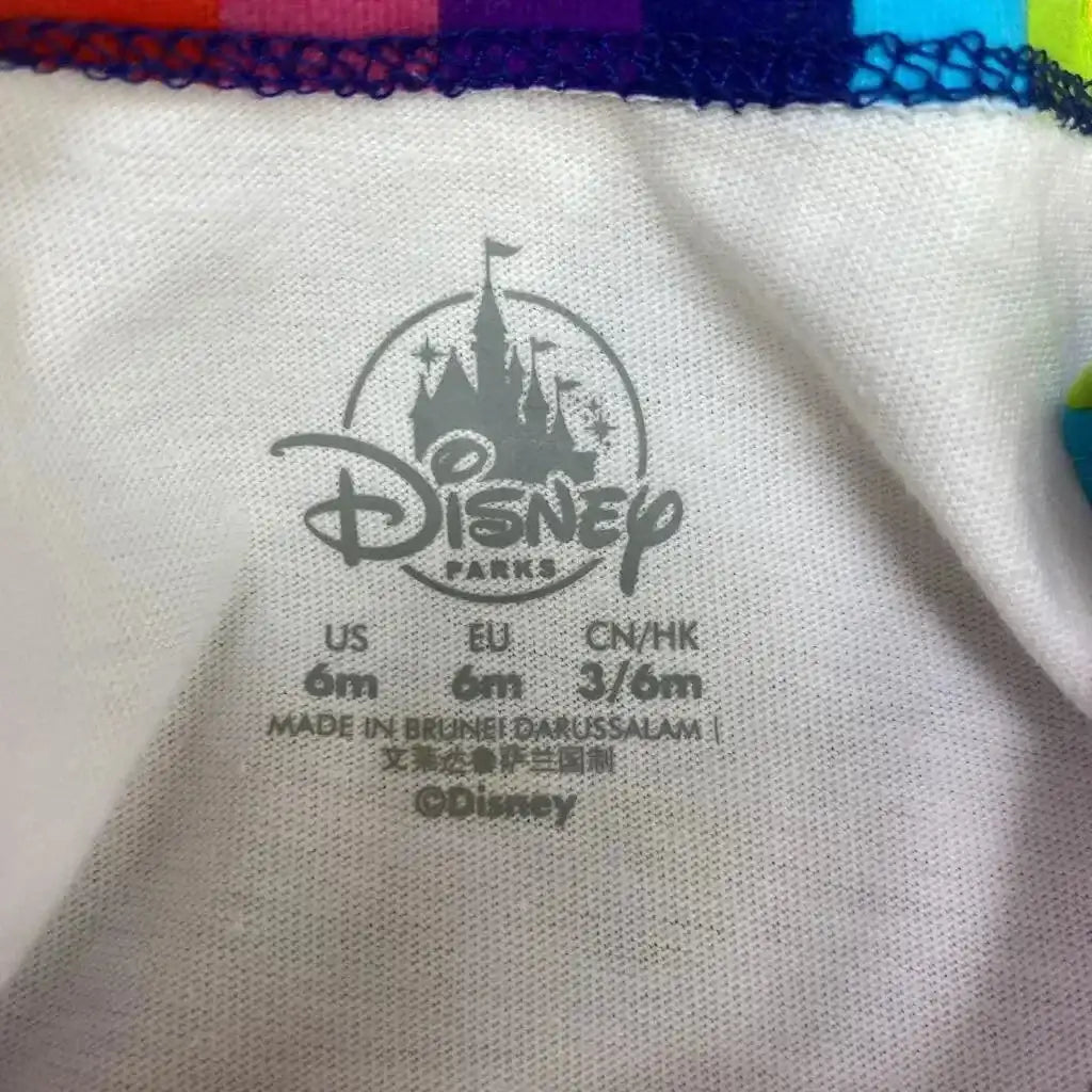 Close-up of white baby bodysuit interior showing Disney Parks logo and printed size 6m with rainbow-trim neckline