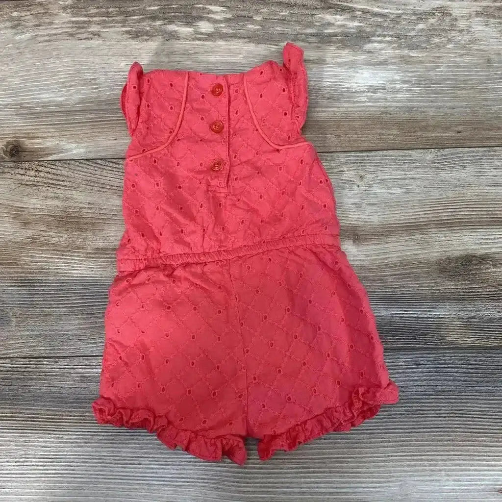 Front view of coral Calvin Klein eyelet romper in size 3 to 6 months with button front and ruffled hems on wood background