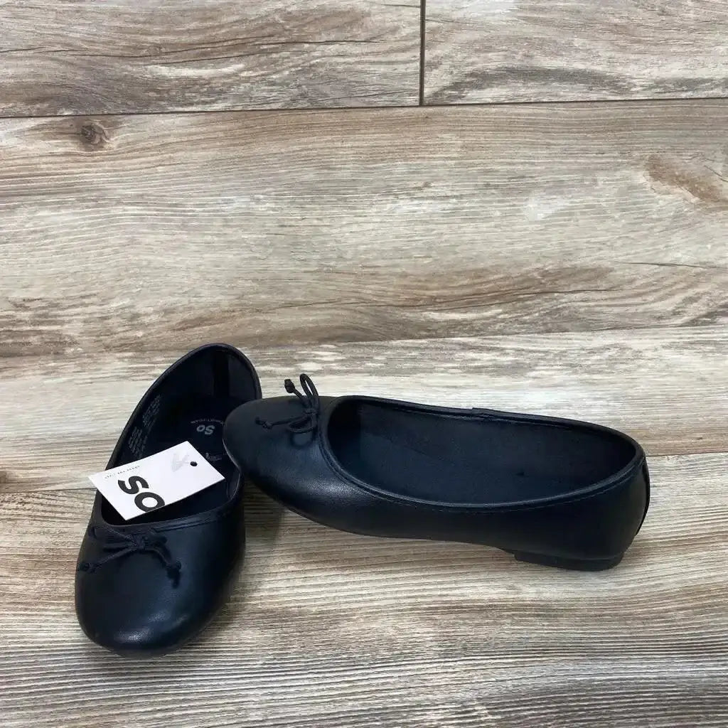 Side and front view of toddler black New SO Pensacola ballet flats showing bow detail and attached SO tag on wood floor background
