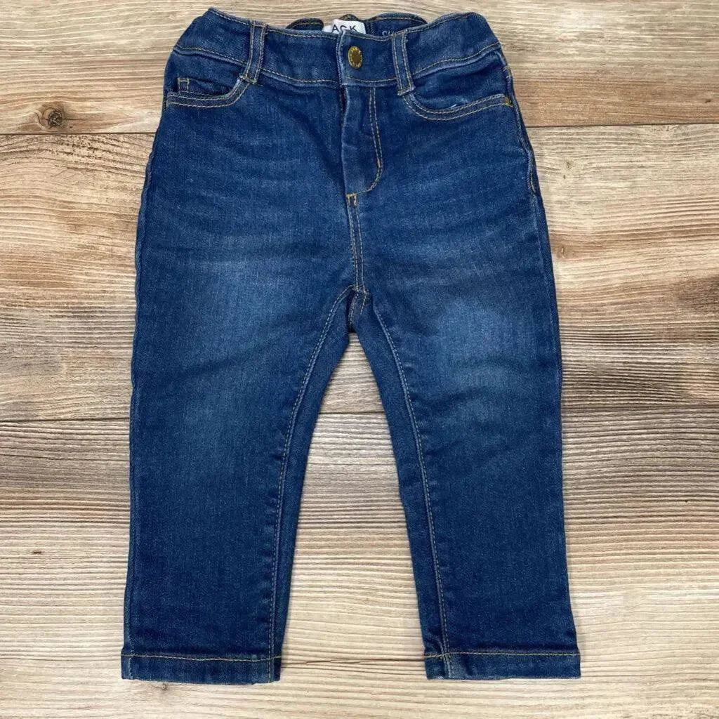 Flat lay of blue toddler skinny jeans (12–18m) showing elastic waistband, faux front pockets, and faded whiskering on wood backdrop