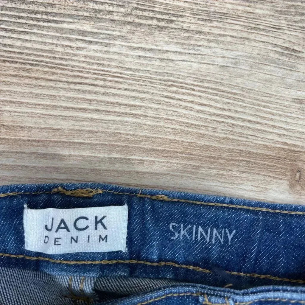 Close-up of blue Jack Denim skinny jeans waistband showing JACK DENIM label and SKINNY print on light wood surface