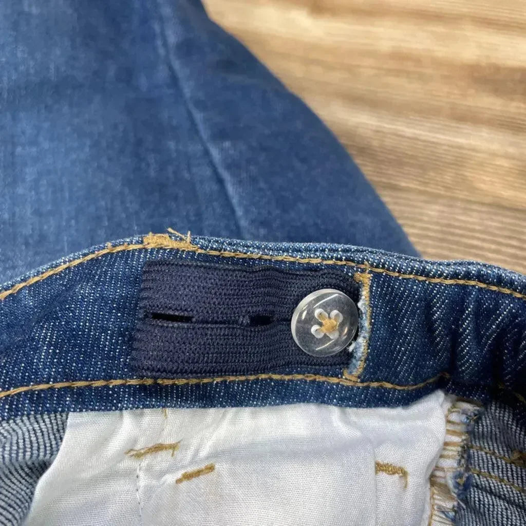 Close-up of blue denim skinny jeans 12 to 18 months showcasing adjustable interior elastic and button with wood floor background