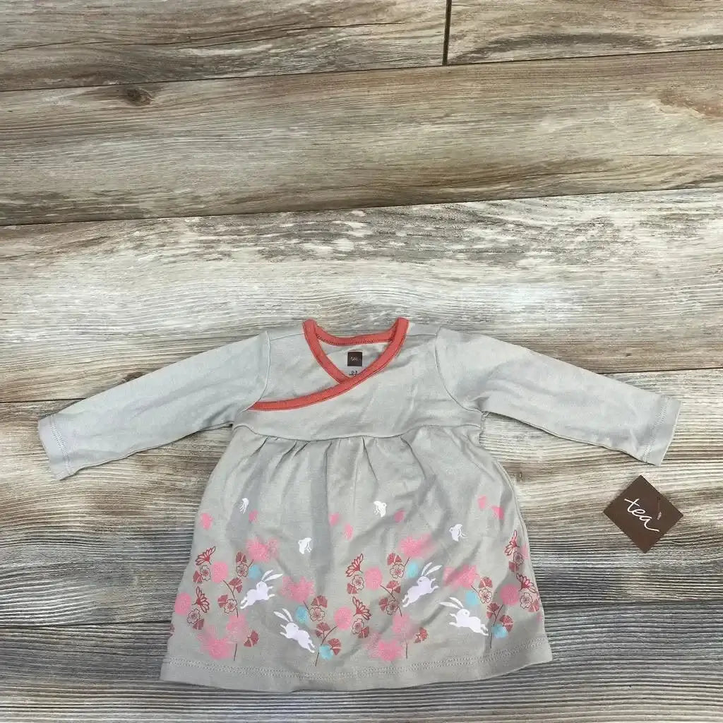 Top-down view of taupe wrap-neck 0-3M baby dress showing coral trim and floral-and-bunny print on wood background