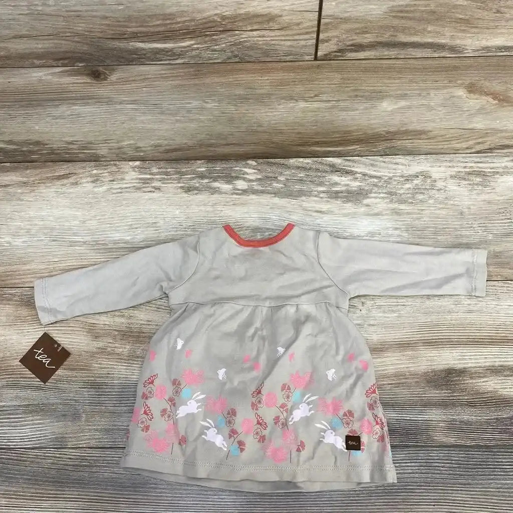 Flat lay of taupe wrap-neck baby dress, 0-3 months, showing long sleeves and pink floral and rabbit print on wood floor