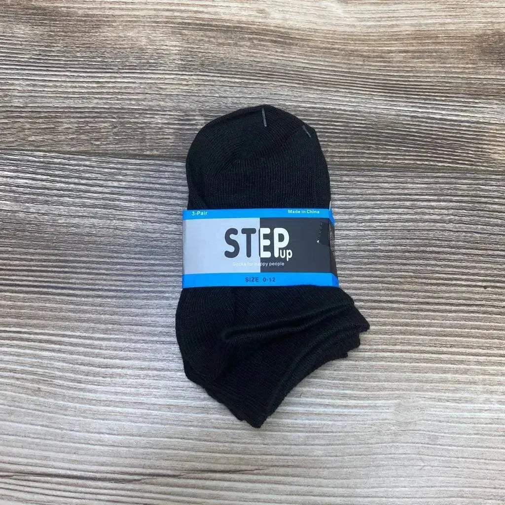 Top-down view of a folded 3-pack of black baby ankle socks showing a blue 'STEP Up' label and size 0-12 on a wood background