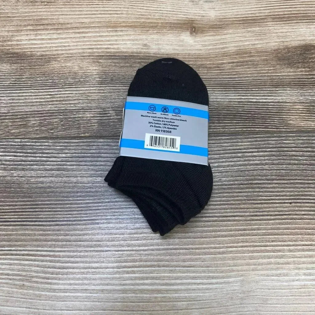 Top-down view of black baby ankle socks 3-pack (0–12 months) showing folded socks with blue and white care label and barcode on a light wood surface