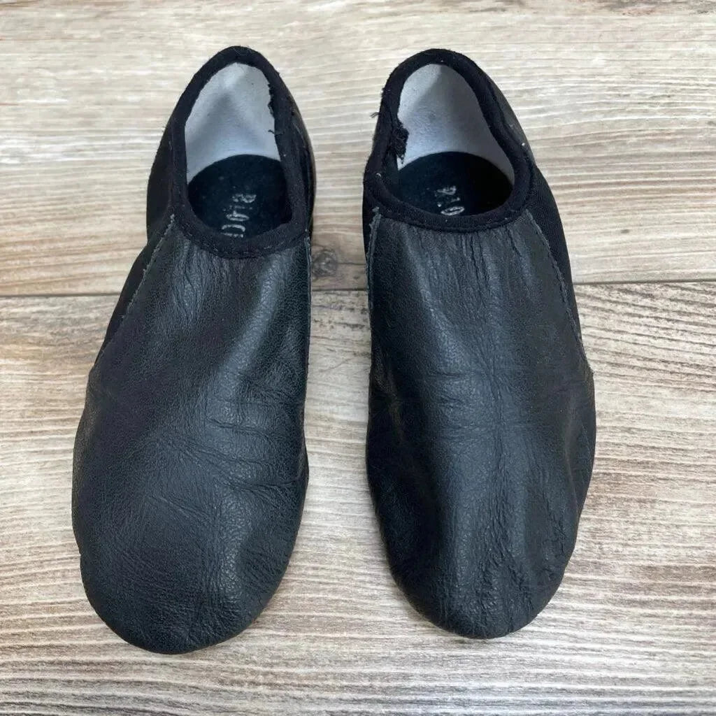 Overhead view of a used pair of black Bloch Neo-Flex slip-on leather jazz shoes with creased uppers and elasticized toplines on a wood floor