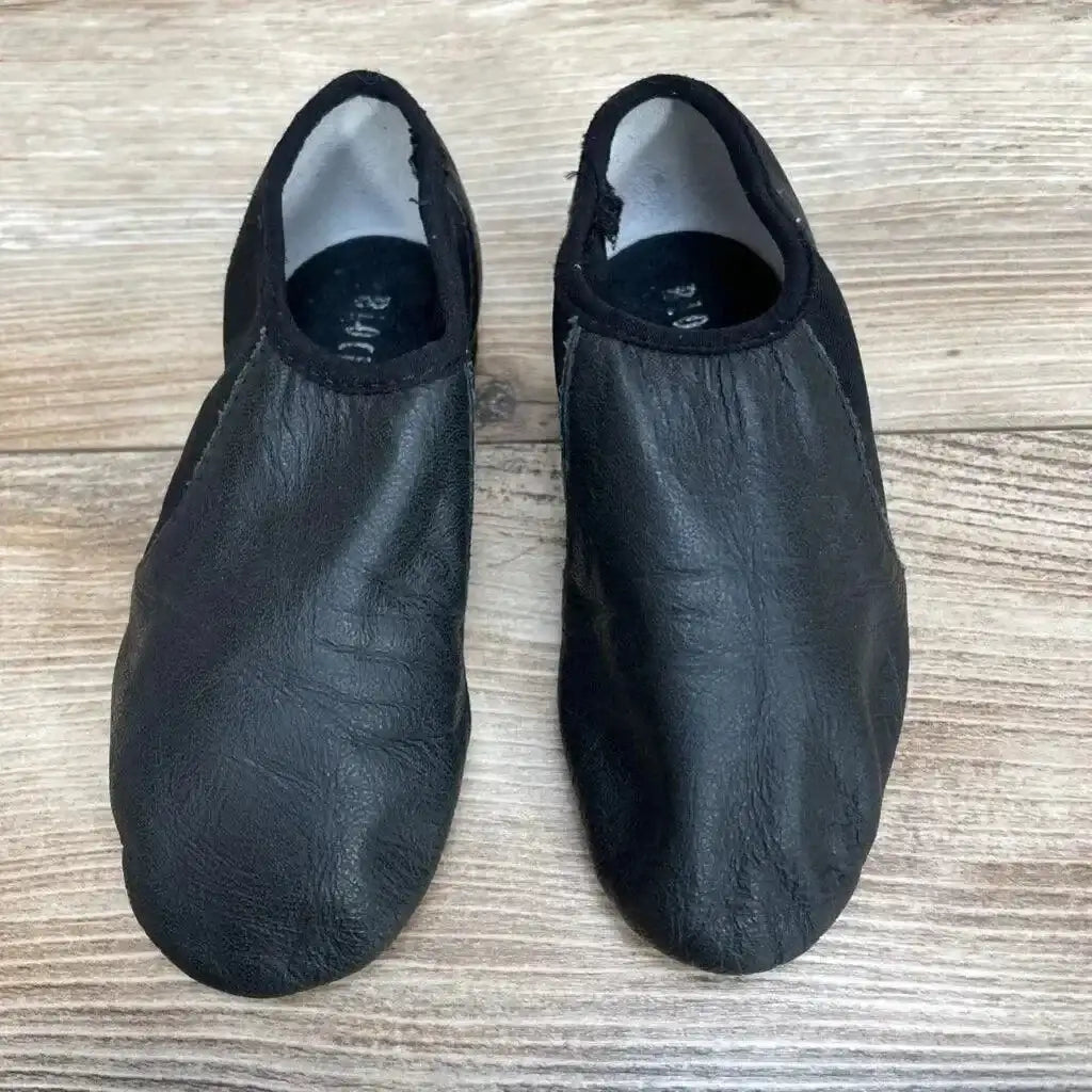 Overhead view of a used pair of black Bloch Neo-Flex slip-on leather jazz shoes with creased uppers and elasticized toplines on a wood floor