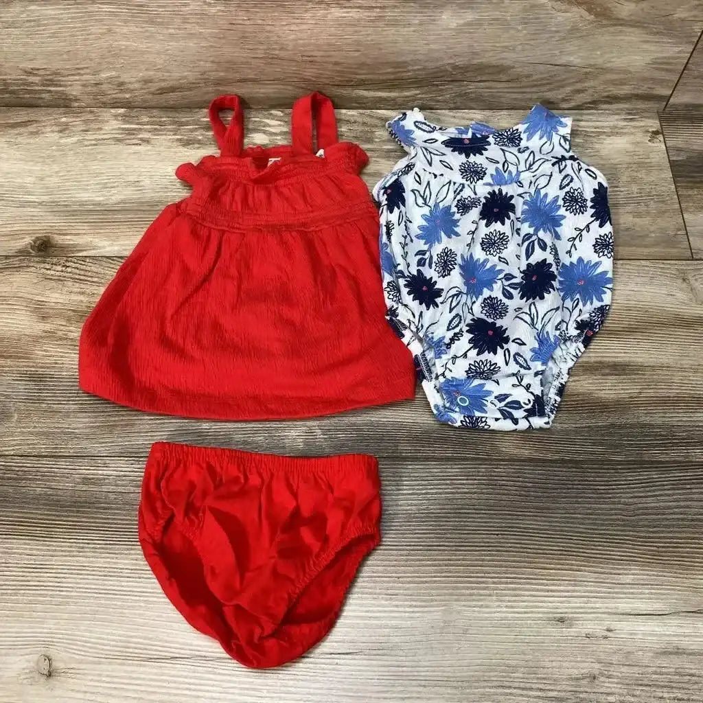 Flat lay of 3-piece baby romper set showing red sleeveless dress, red bloomers, and white-blue floral romper on wood floor