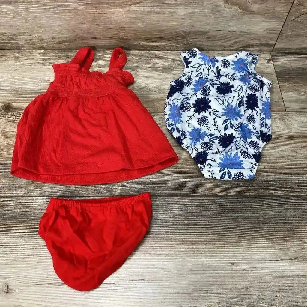 Flat lay of 3-piece baby set showing white and blue floral sleeveless romper with red sleeveless dress and matching red diaper cover on wood background