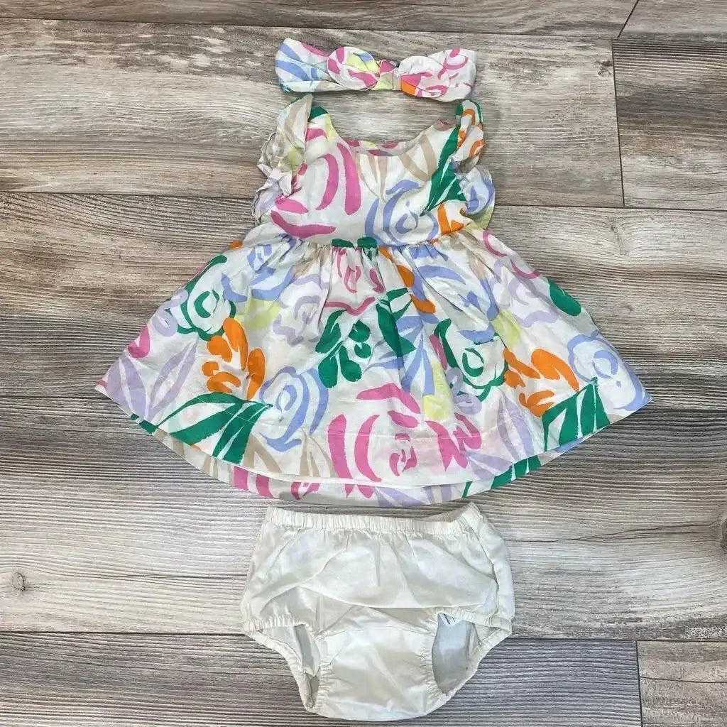 Flat lay of BabyGap 3-piece tropical dress with headband and white bloomers, multicolor floral print and ruffle sleeves on wood floor