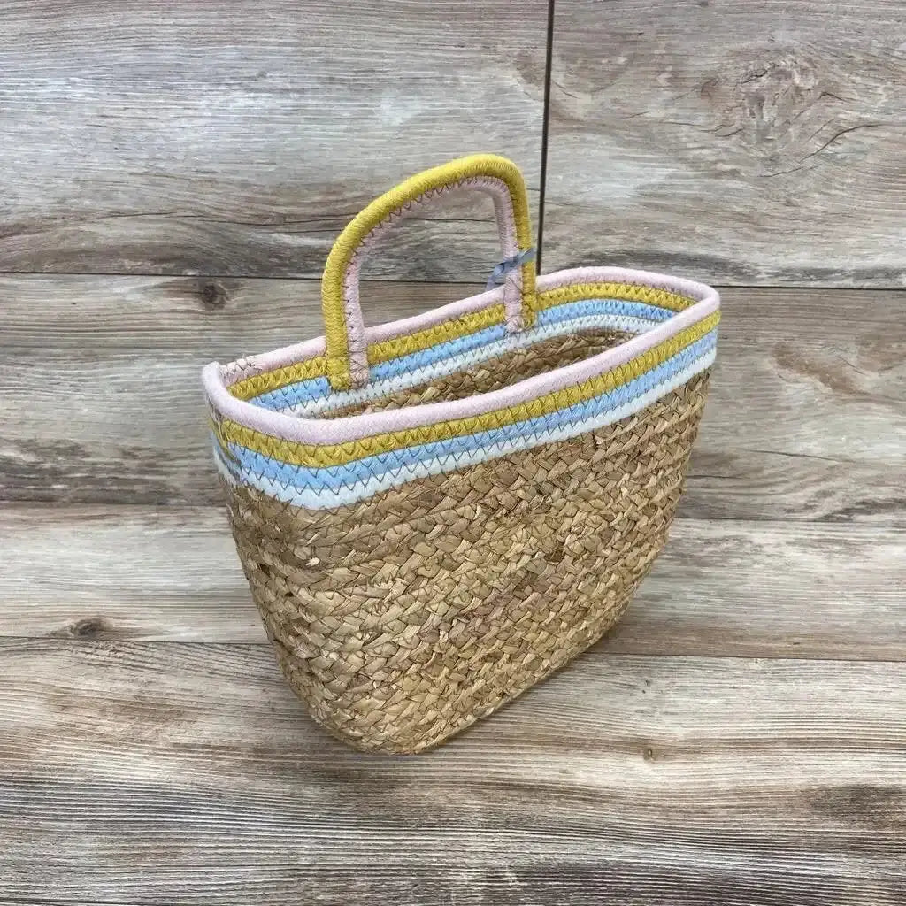 Three-quarter view of woven wall-hanging basket showcasing pastel pink, yellow, and blue coiled rope trim and handle on wooden background