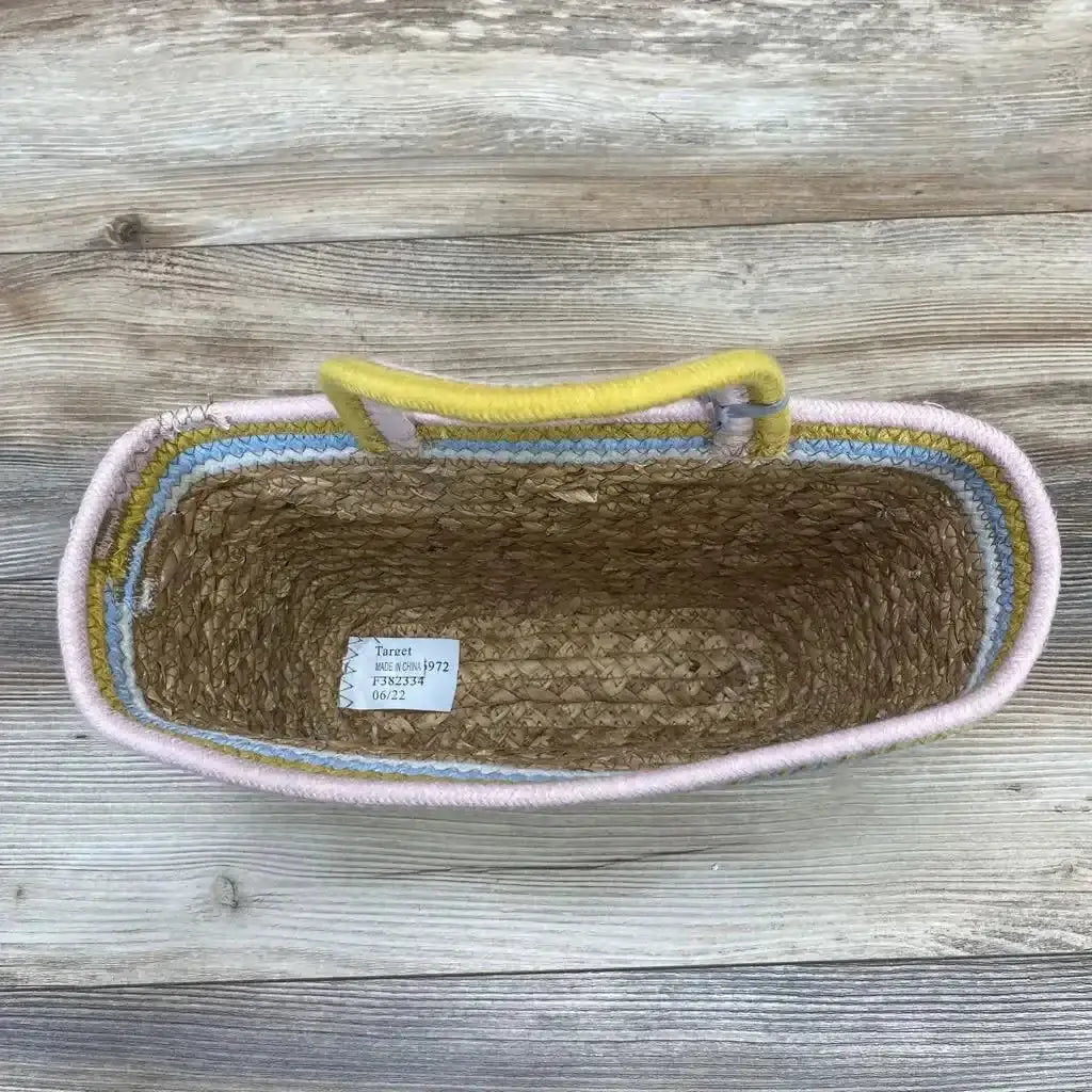 Top-down view of brown woven wall-hanging basket with pastel pink, blue and yellow rim and yellow rope handle on wood